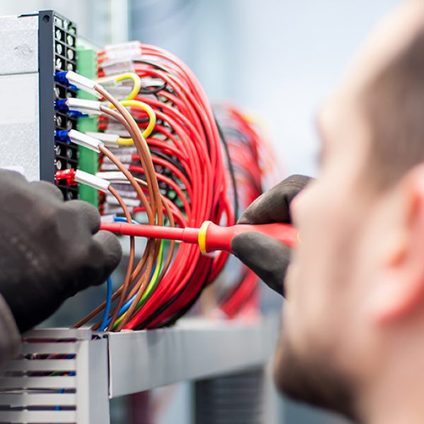 Closeup of electrician engineer works with electric cable wires of fuse switch box. Electrical equipment